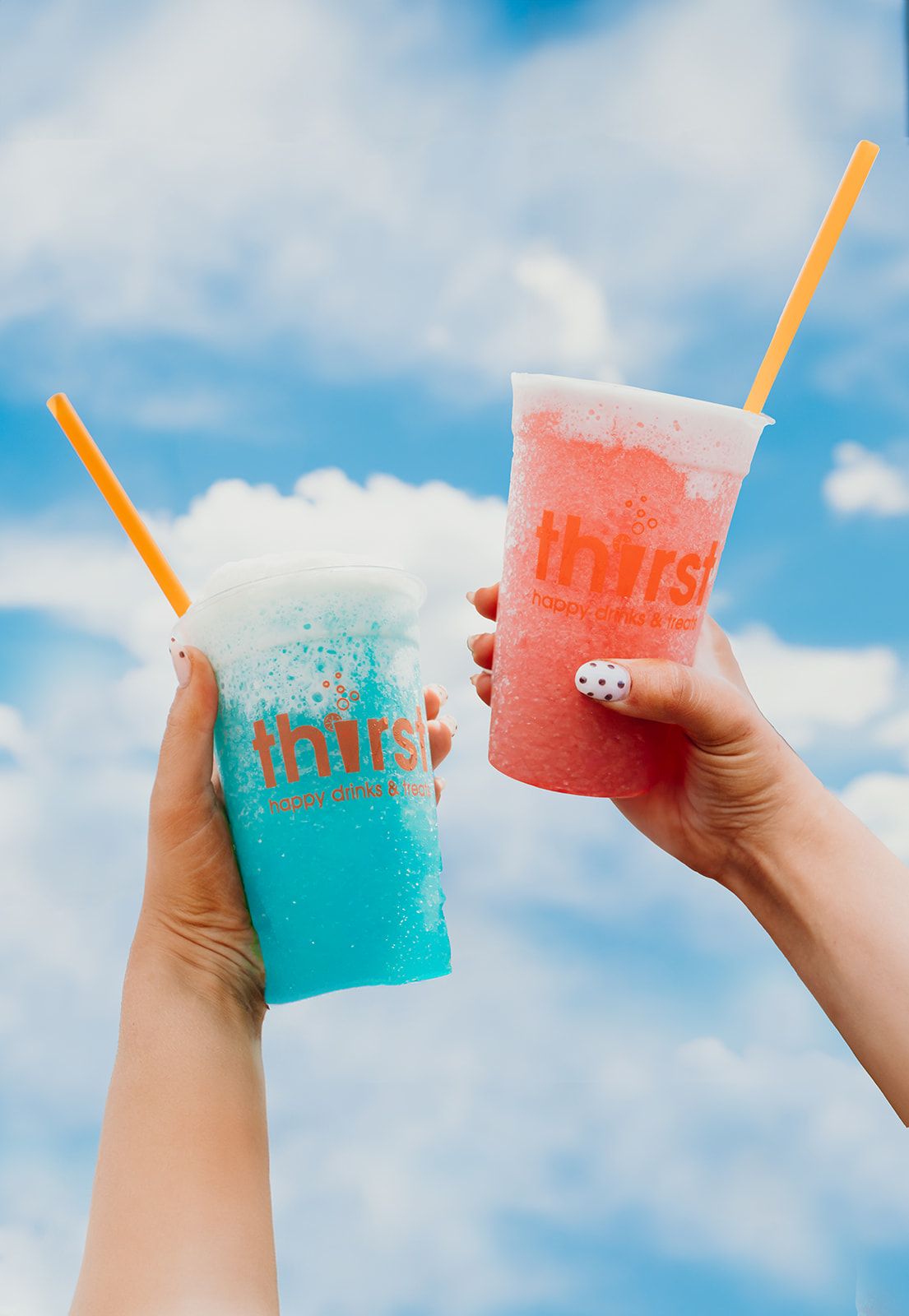 Two hands toasting Thirst slushie cups against a blue sky