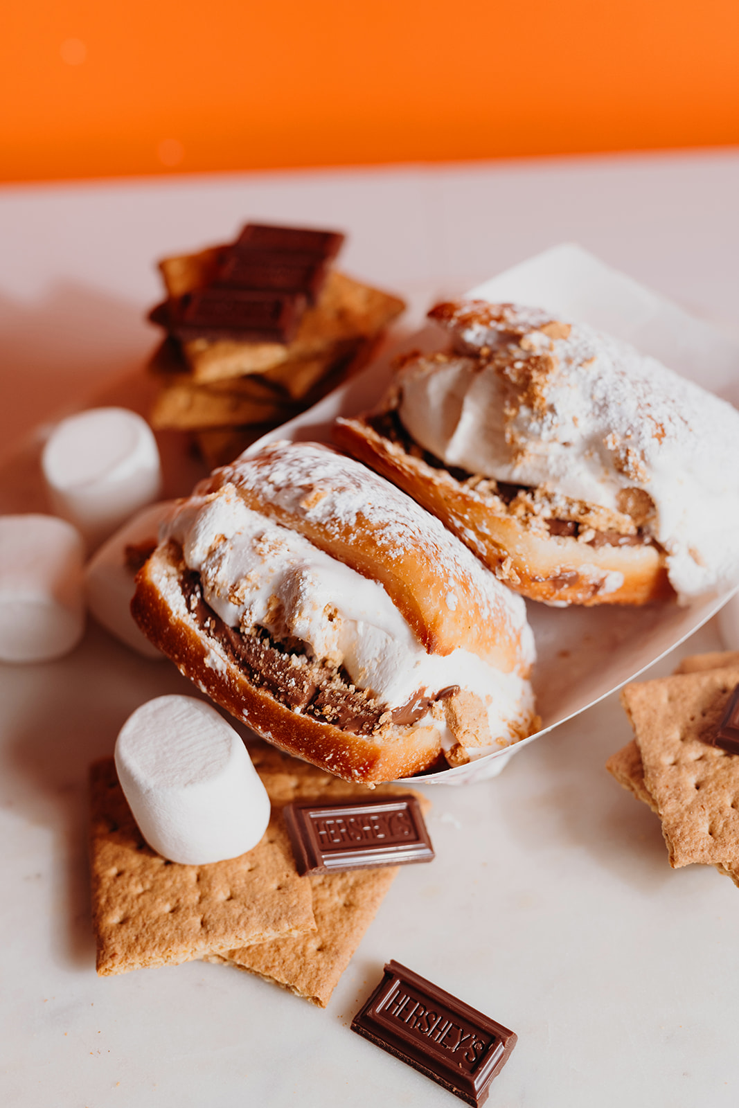 S'more Beignets in a paper tray — beignets filled with chocolate and marshmallow fluff, topped with graham cracker crumb and powdered sugar