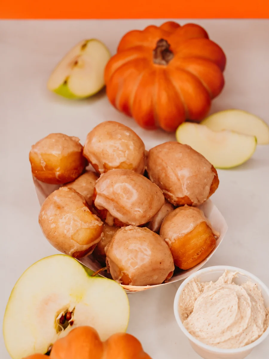 Apple cider glazed beignet bites with the included apple cinnamon cream cheese dip, surrounded by sliced apples and pumpkins