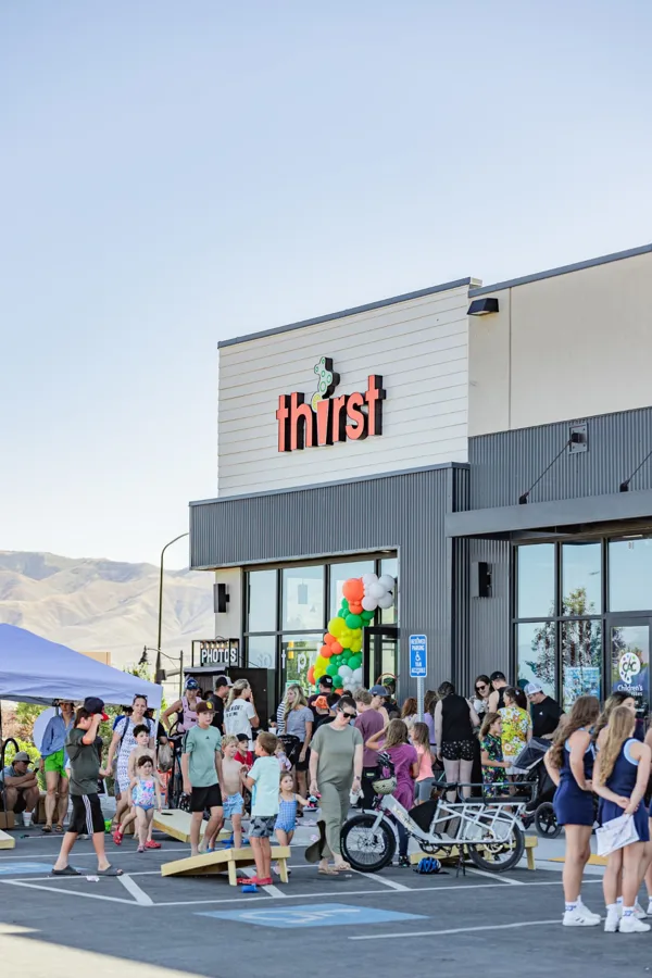 Families playing cornhole outside a new Thirst store on grand opening day
